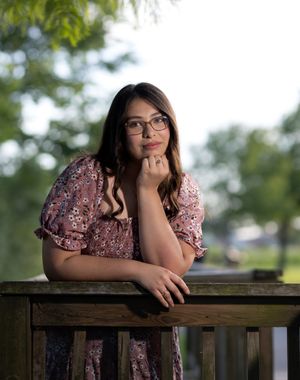 Outdoor portrait of model leaning on wooden fence at golden hour.
