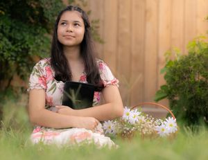 A person in a pink floral dress sits in a garden with daisies, looking thoughtfully upward against a wooden fence. In Pearland, TX