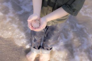 Hands holding wet sand on a beach shore with waves lapping at their feet in soft focus.In Galveston, TX