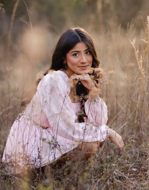 Young woman in pink floral dress sitting gracefully among golden wild grasses in a sunlit outdoor field.