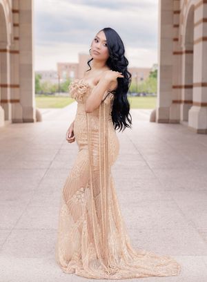 Woman in elegant gold sequin mermaid gown posing gracefully between stone columns at an outdoor venue.