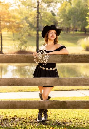 Rustic autumn portrait session at a wooden fence with soft golden sunlight filtering through trees in the background.