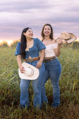 Two friends in denim jeans share laughter while posing together in a sunlit meadow at golden hour.