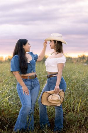Two friends in matching denim outfits share laughter in a sunlit meadow at sunset.