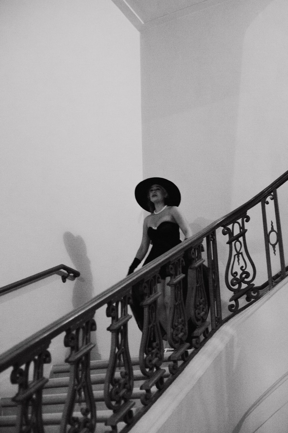 Figure in a hat ascending ornate stairs in a dramatic black and white composition.