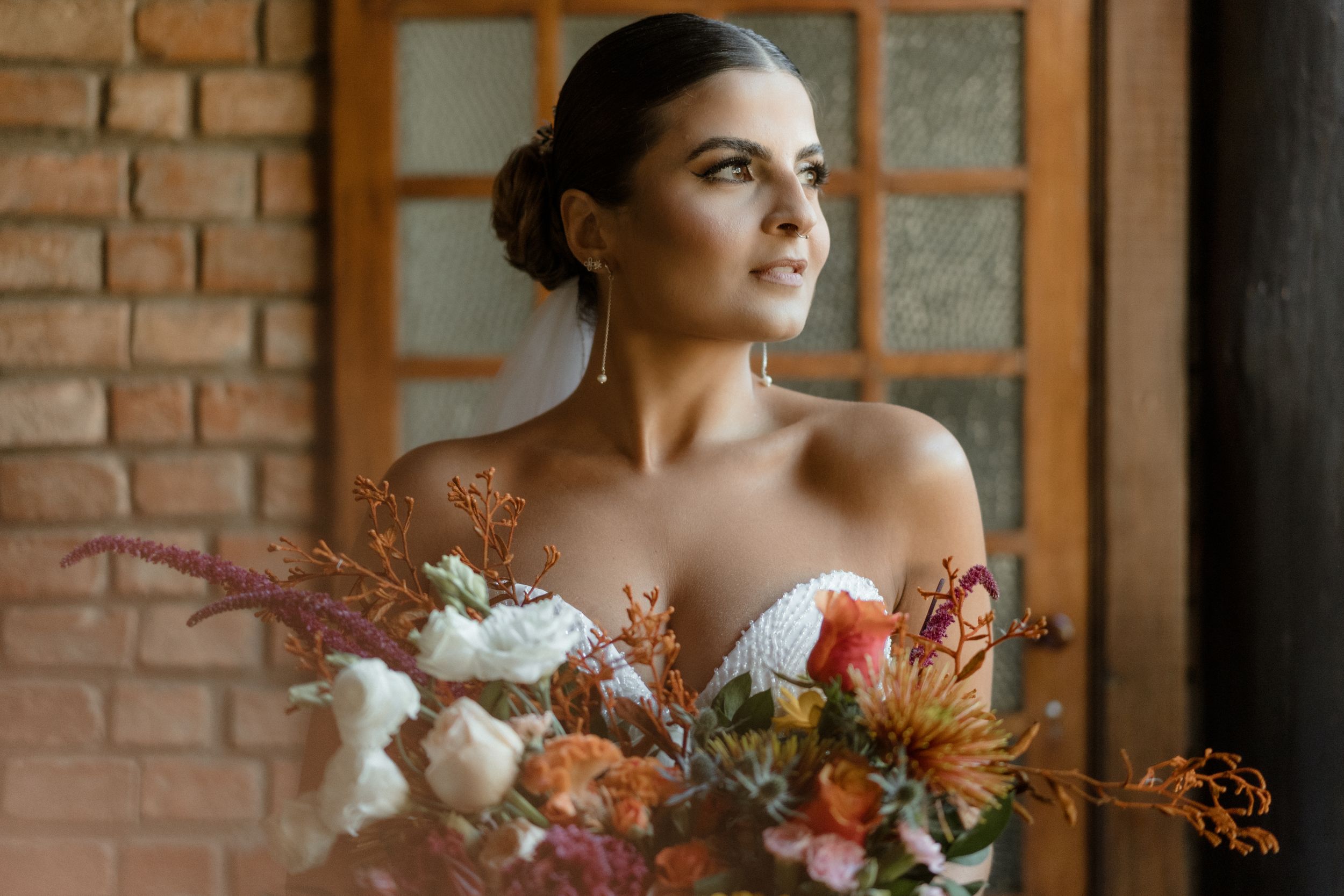 Elegant bridal portrait against exposed brick wall with autumn-toned floral bouquet.