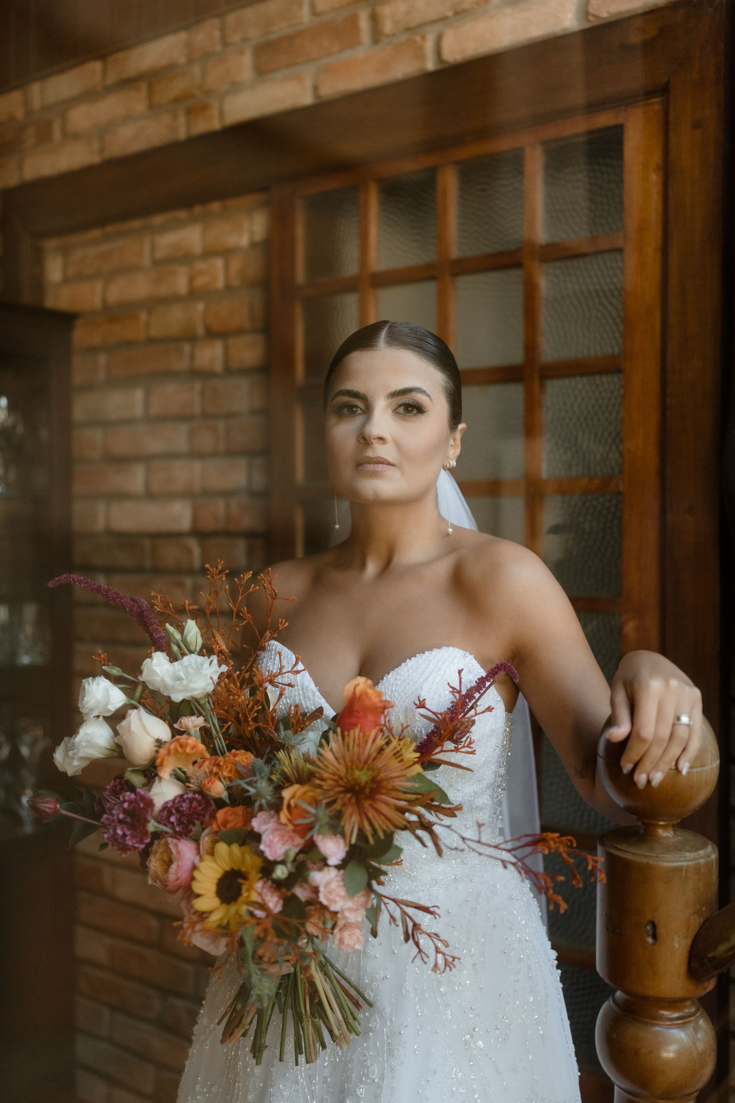 Wedding dress details with rustic decor and fall-colored florals against brick wall.
