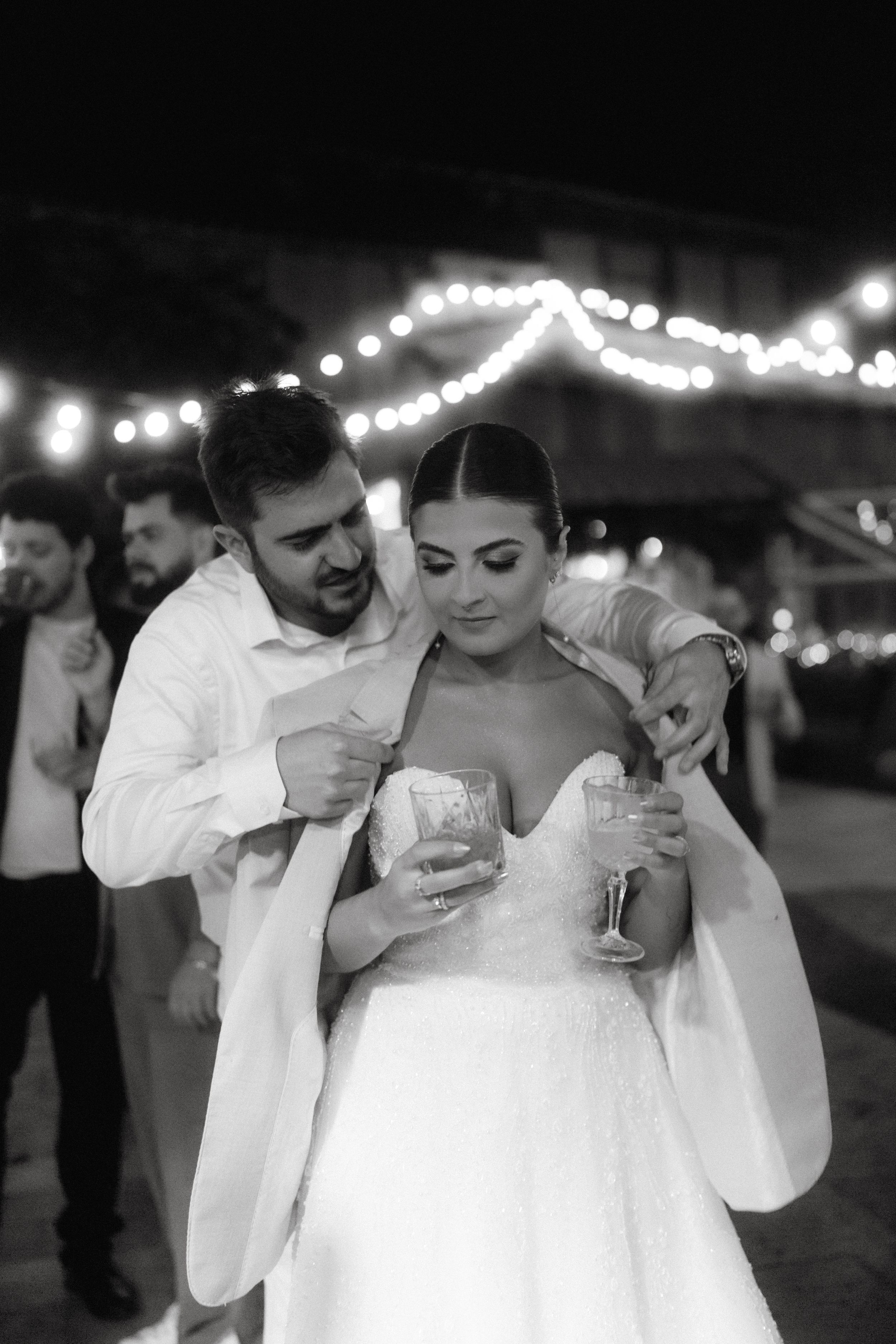 A romantic moment on the dance floor under twinkling string lights at an outdoor wedding reception.