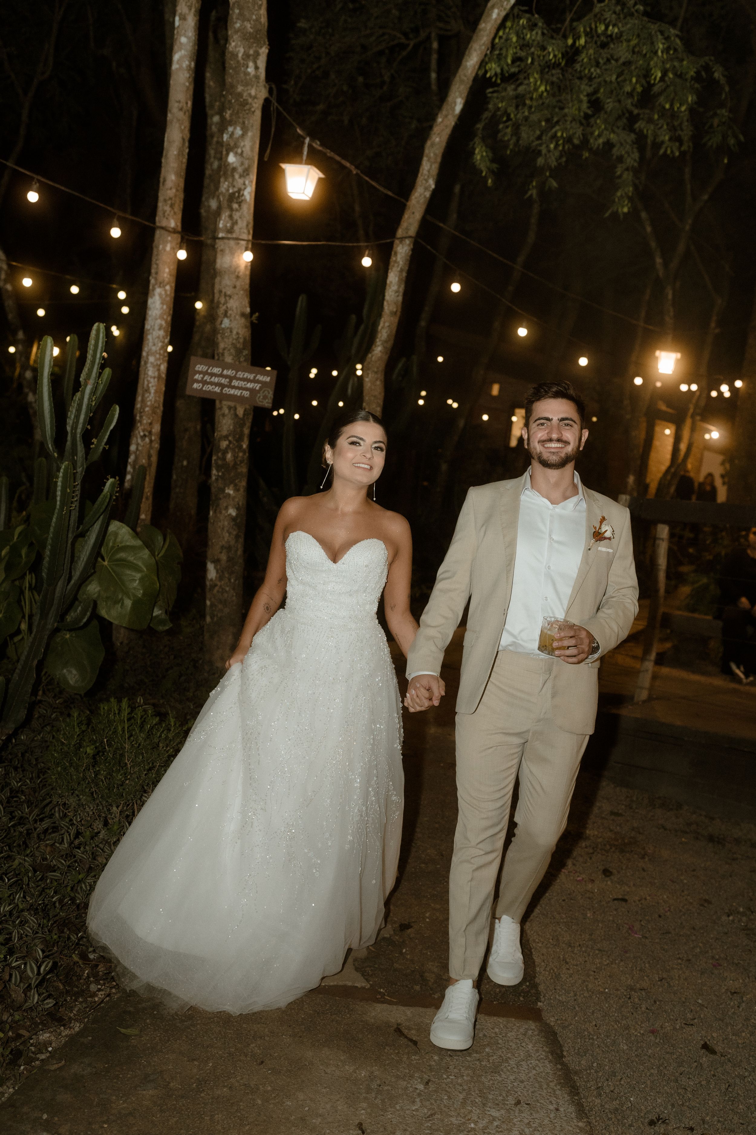 A couple walking along a path lit by string lights at night with trees in the background.