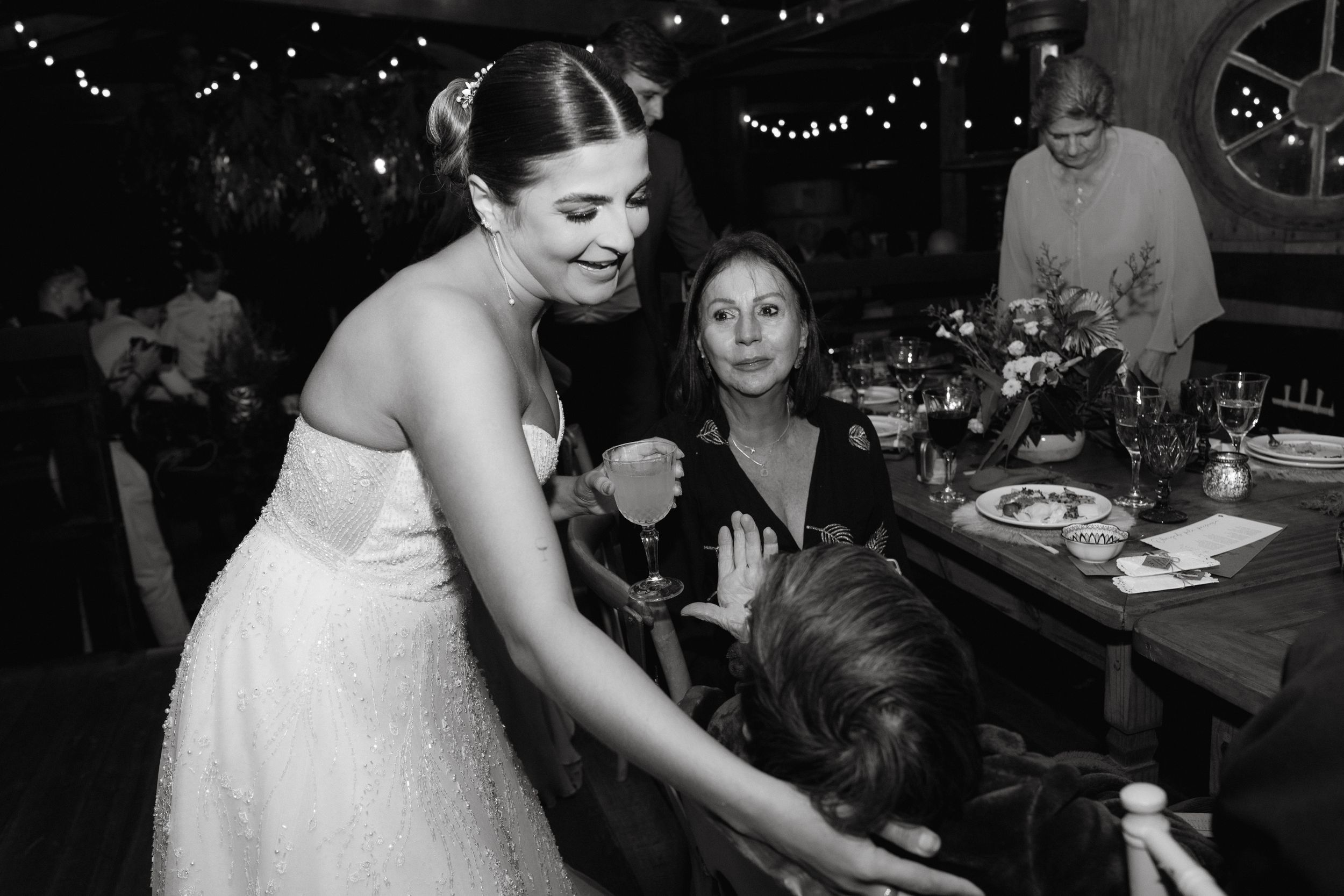 Wedding reception scene with guests seated at tables under string lights.