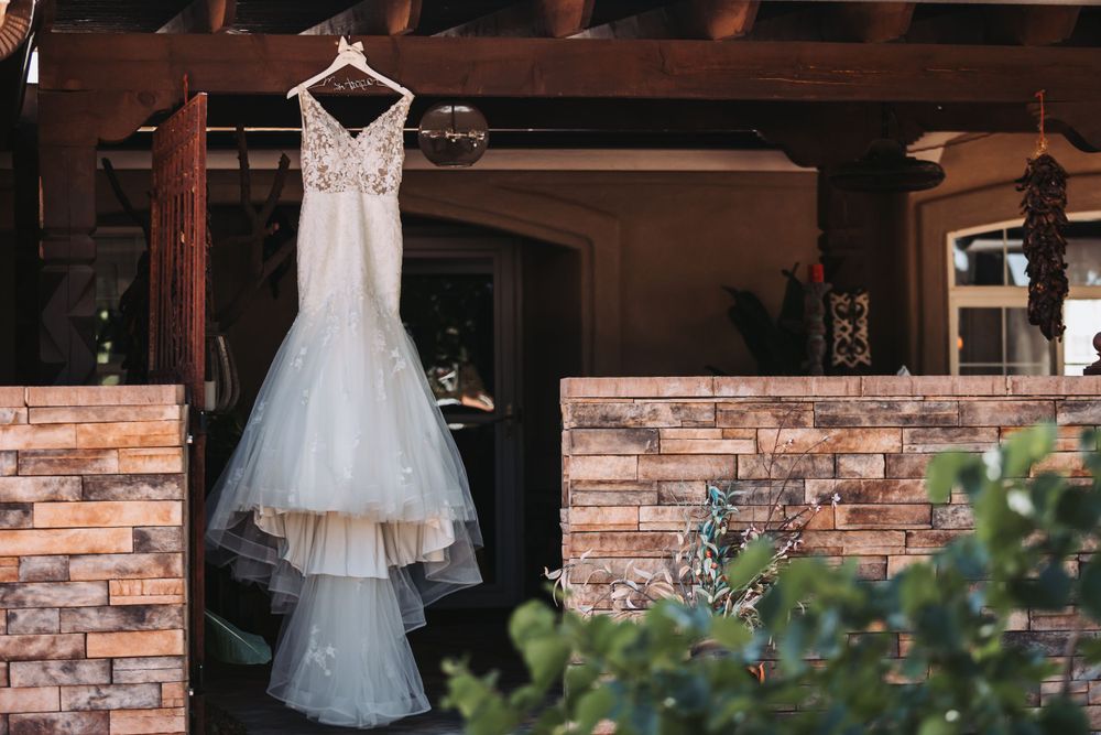 An elegant white lace wedding dress hangs on display against a rustic stone wall exterior.