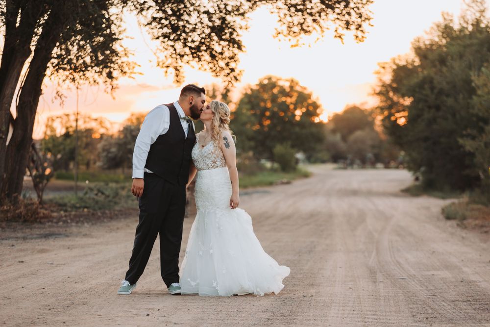 Newlyweds share an intimate moment on a dirt road at sunset with trees in the background.