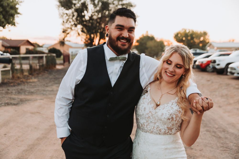 Happy wedding couple laugh together on a rustic dirt path during golden hour.