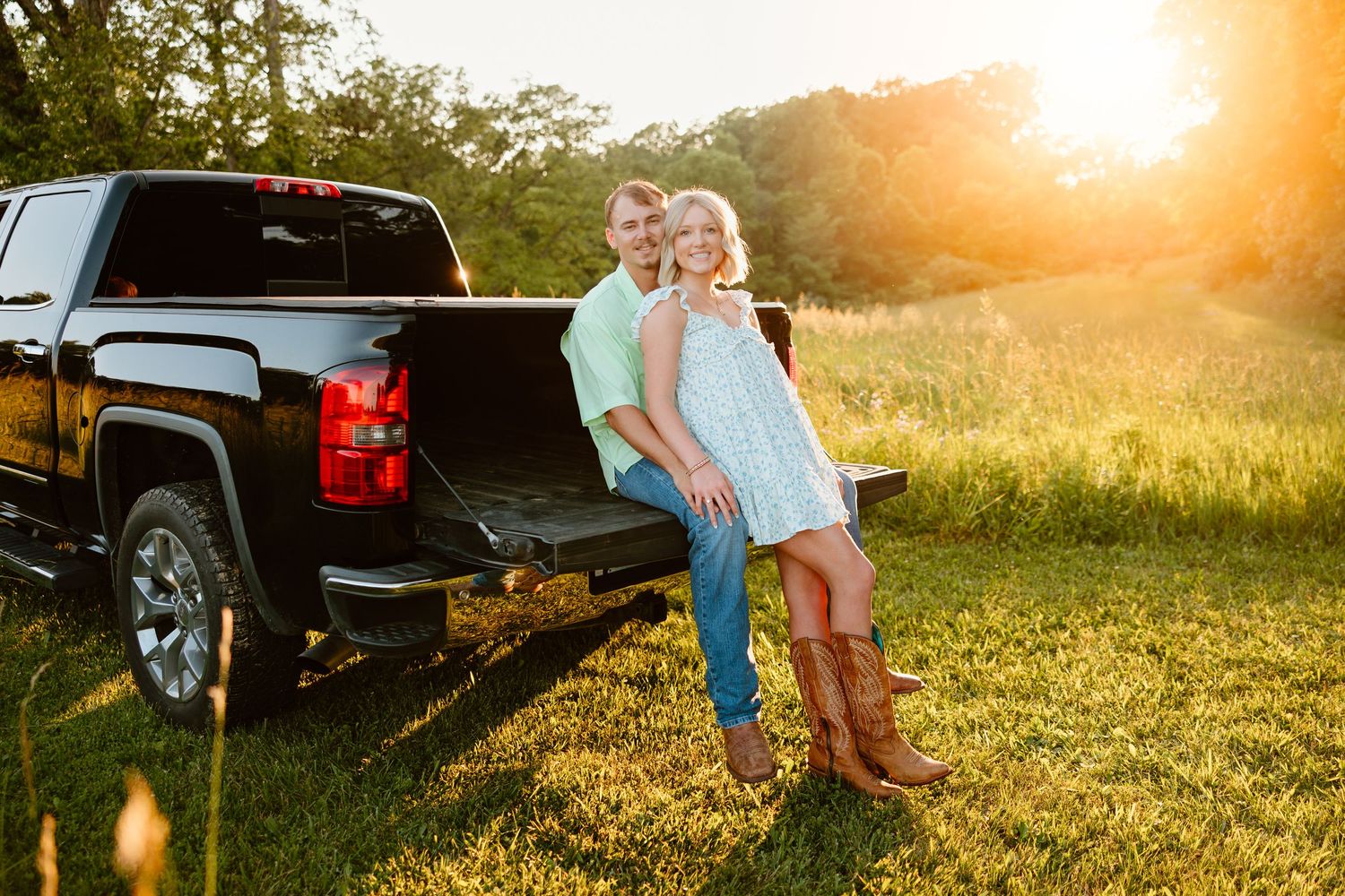 Sunset silhouette of couple by pickup truck in grassy field.