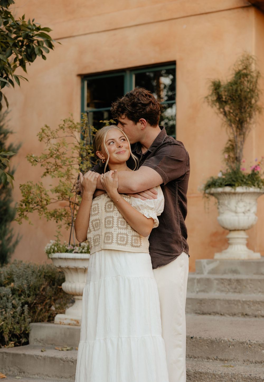 Man kissing woman on cheek while embracing outside a rustic villa.