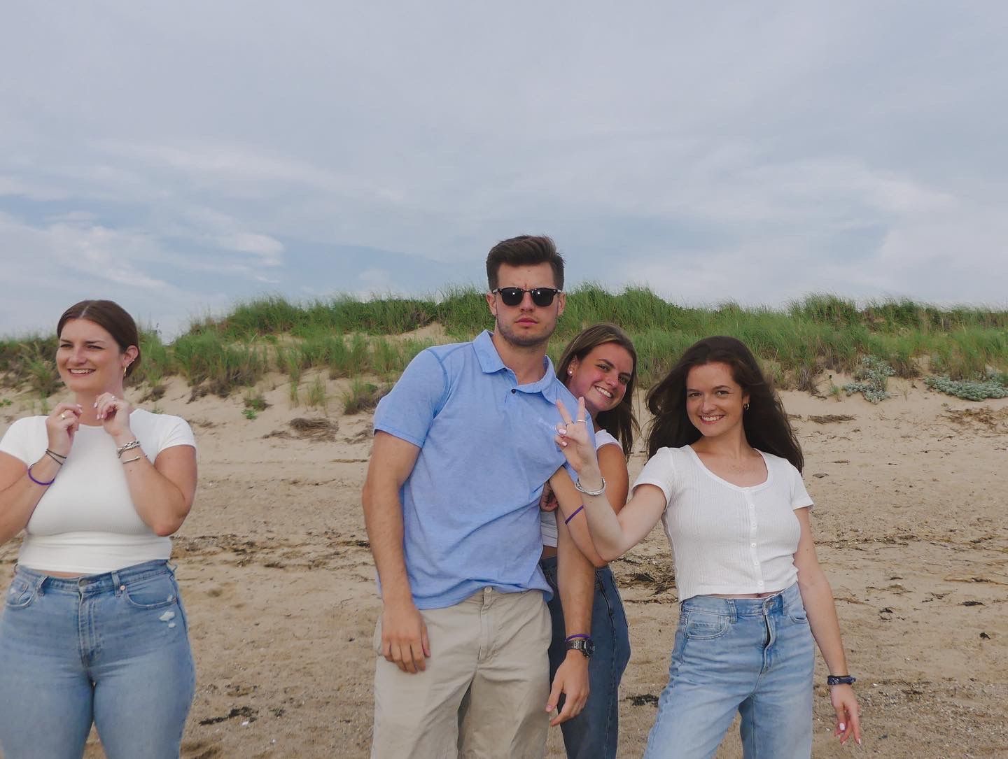 Group of four friends posing and smiling on a sandy beach.