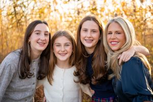 Four people smiling together outdoors during golden hour with autumn foliage in the background.