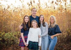 A family poses together in a golden field during autumn sunset wearing coordinated casual outfits.