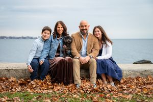 A group sits together on fallen autumn leaves by the ocean shore during a casual outdoor photo session.