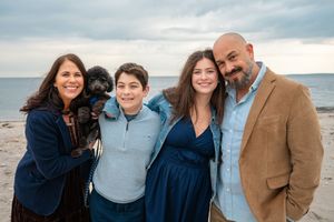 A family wearing coordinated navy and tan outfits poses together for photos on a cloudy beach.