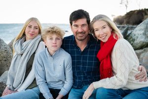 Family group sits together on coastal rocks near the ocean during a photo session.