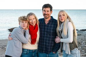 Family group enjoying a casual beach photoshoot together on a sunny day by the ocean.