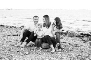 A black and white photo of a family sitting together on a rocky beach at the water's edge.