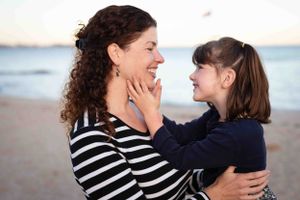 Mom and daughter share a tender moment while laughing together at sunset on the beach.
