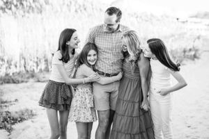 A black and white outdoor portrait of a family of five smiling together against a blurred background.
