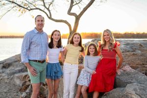 A family poses together on rocky terrain at sunset with a tree silhouetted behind them.