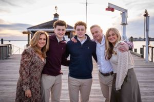 A group of people smiling together while standing on a wooden pier at sunset by the ocean.