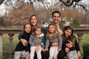 A family smiles together while sitting on a stone railing in a park during autumn.