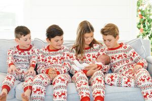 A group wearing matching red and white Nordic print holiday pajamas sits together on a couch looking at a baby