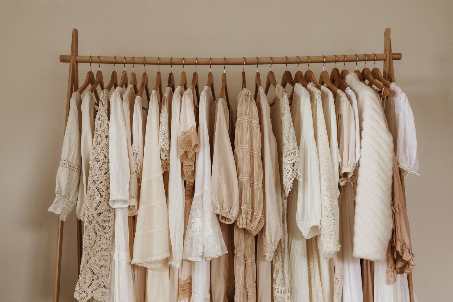 A wooden clothing rack filled with white and cream colored vintage-style dresses and garments.