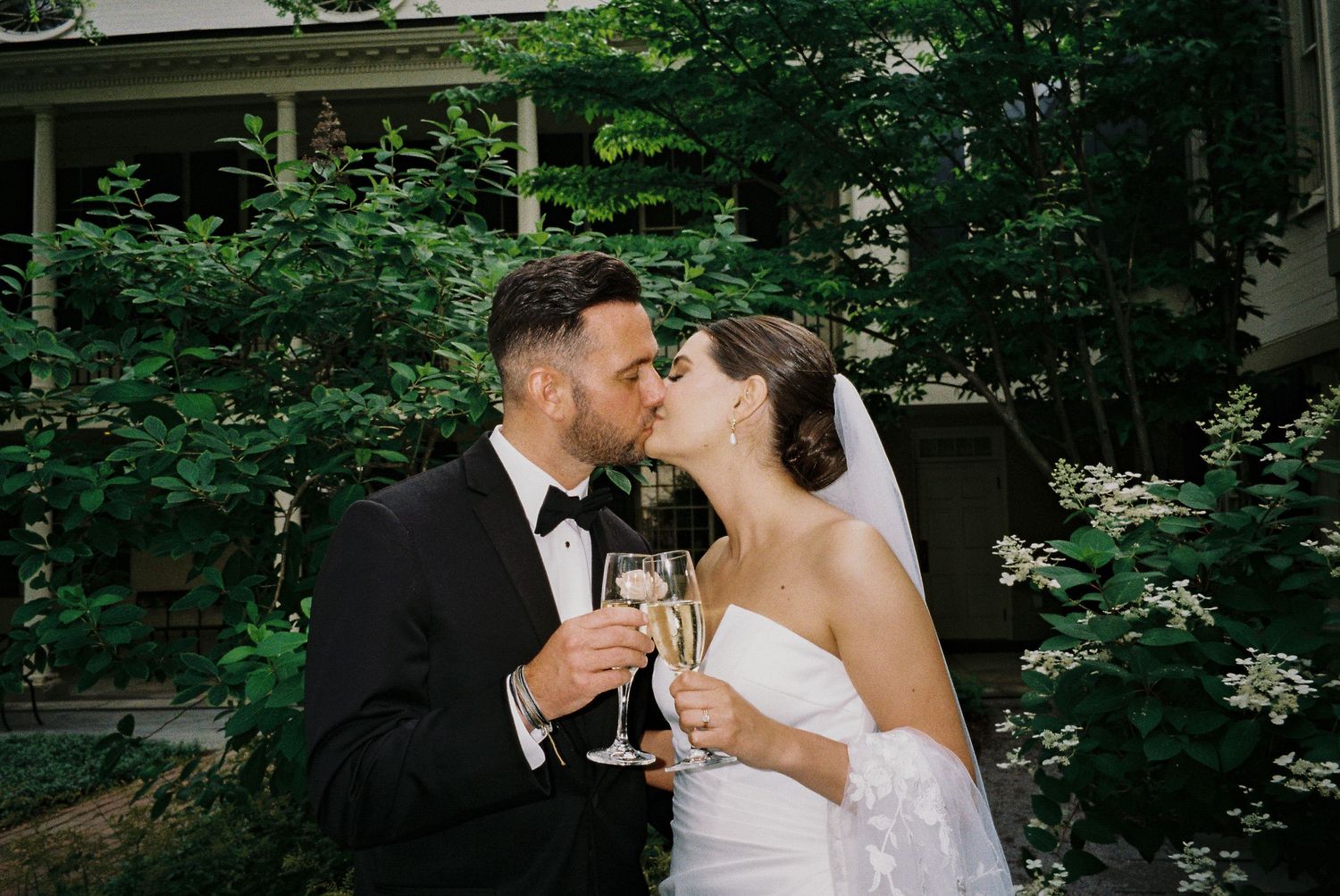 Newlyweds share champagne toast outdoors surrounded by lush greenery.