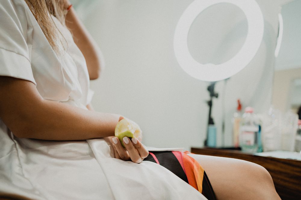 Bride waiting for her makeup, casually eating an apple, capturing a candid pre-wedding moment