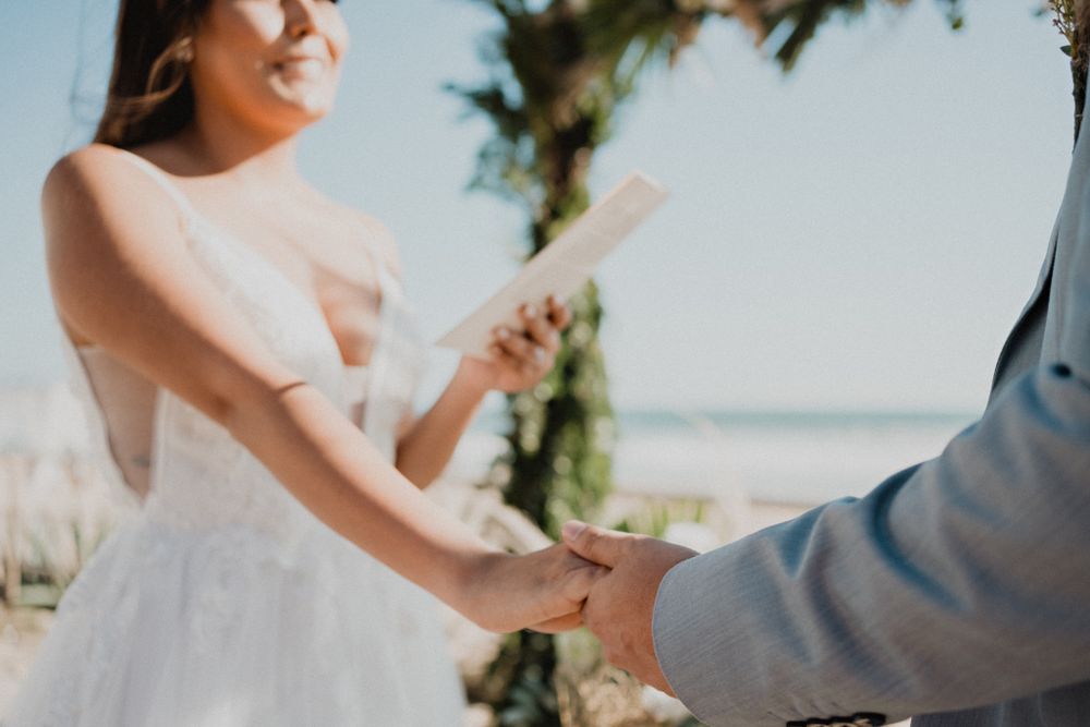 Bride holding the groom's hand while reading her vows, an intimate and emotional wedding moment