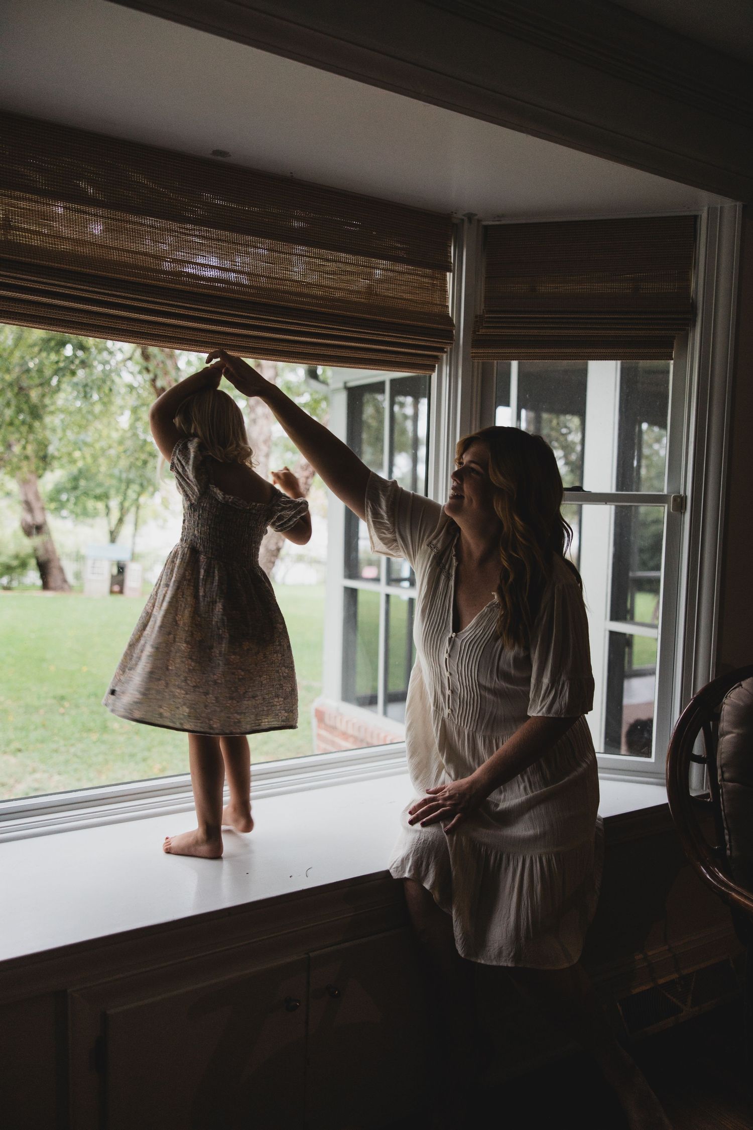 Dancing together by the window in vintage dresses with natural light streaming in.