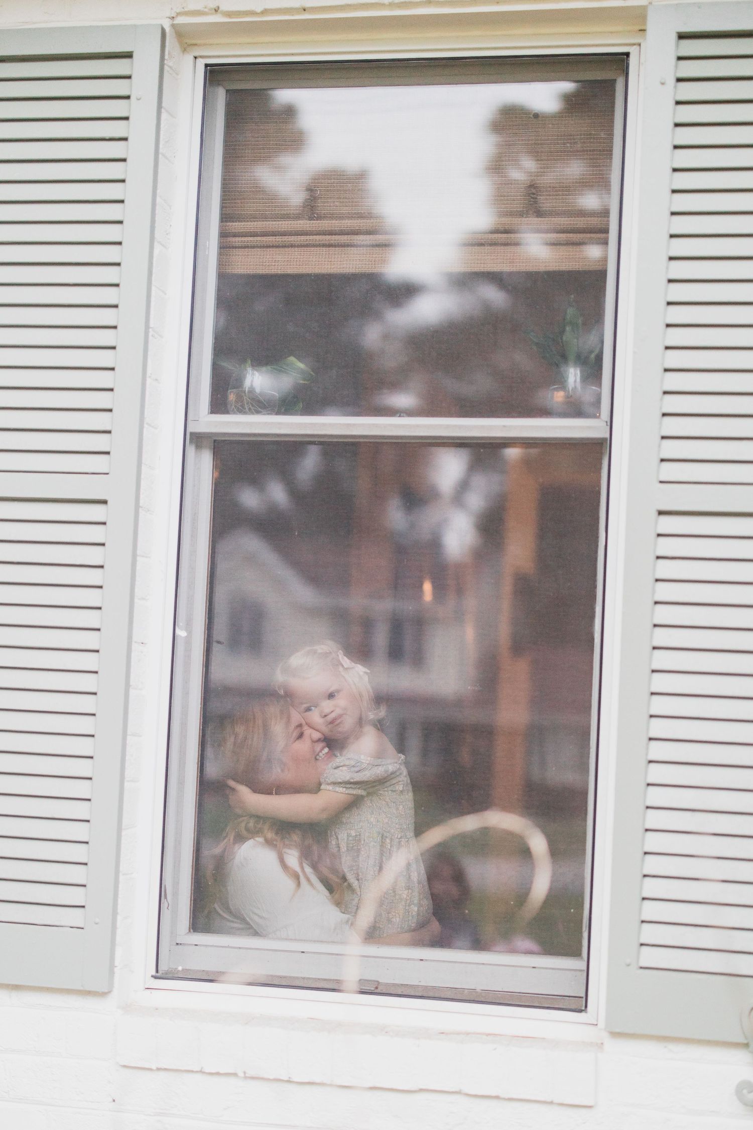 View through window with white shutters showing silhouettes in dreamy soft focus.