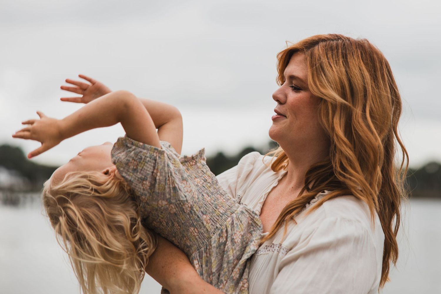 Playful moment captured between parent and child against waterfront setting.