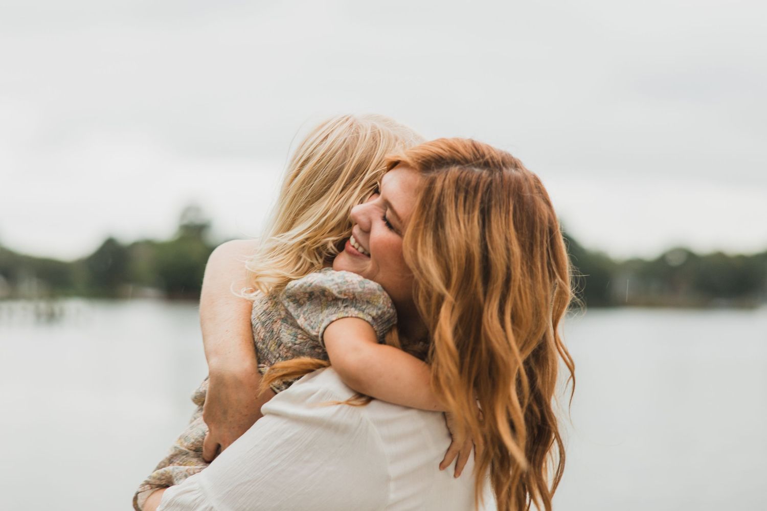 Candid moment of affection between two people laughing on a dock by a lake.
