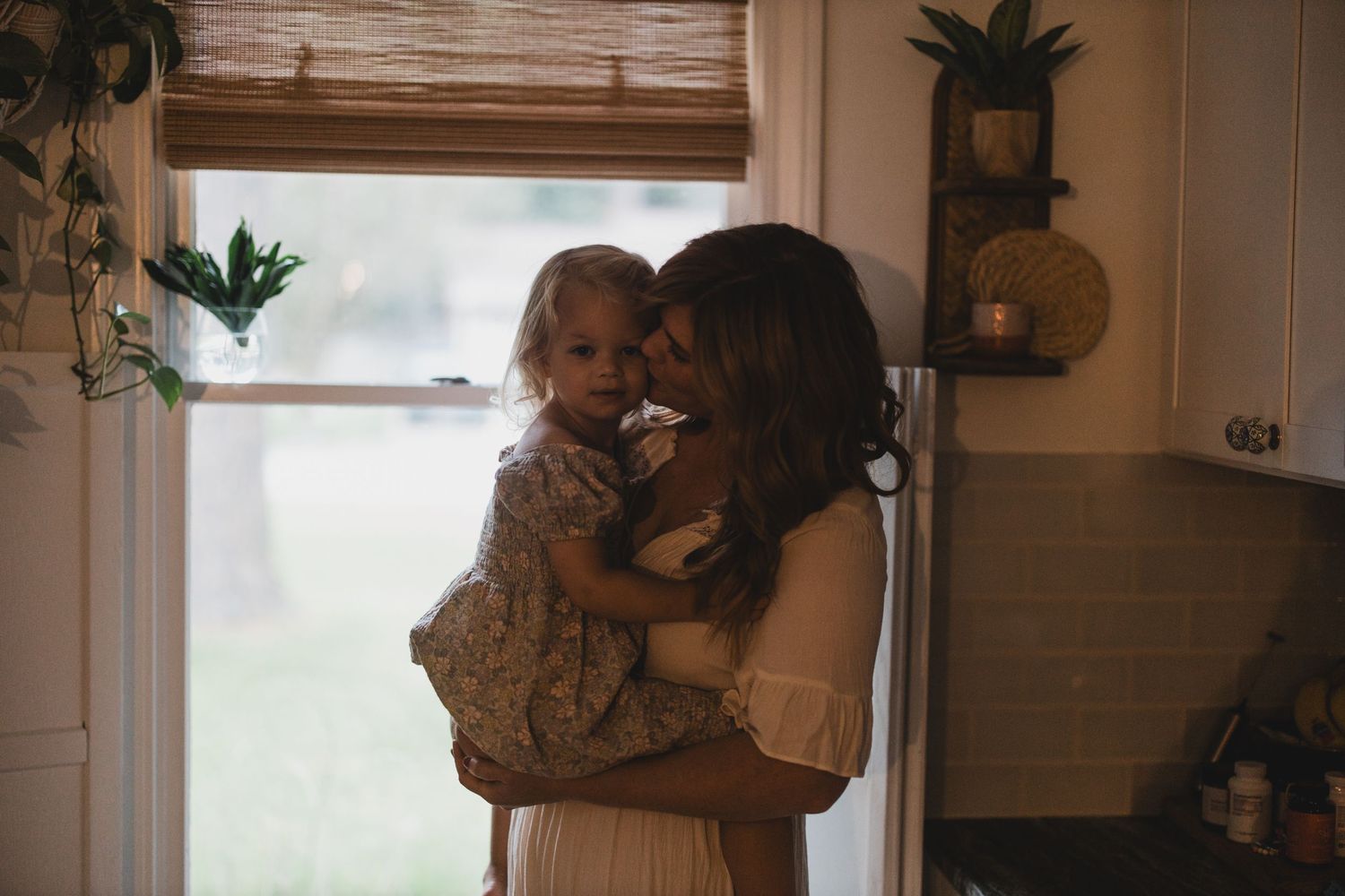 Tender moment captured by window with warm lighting and indoor plants.