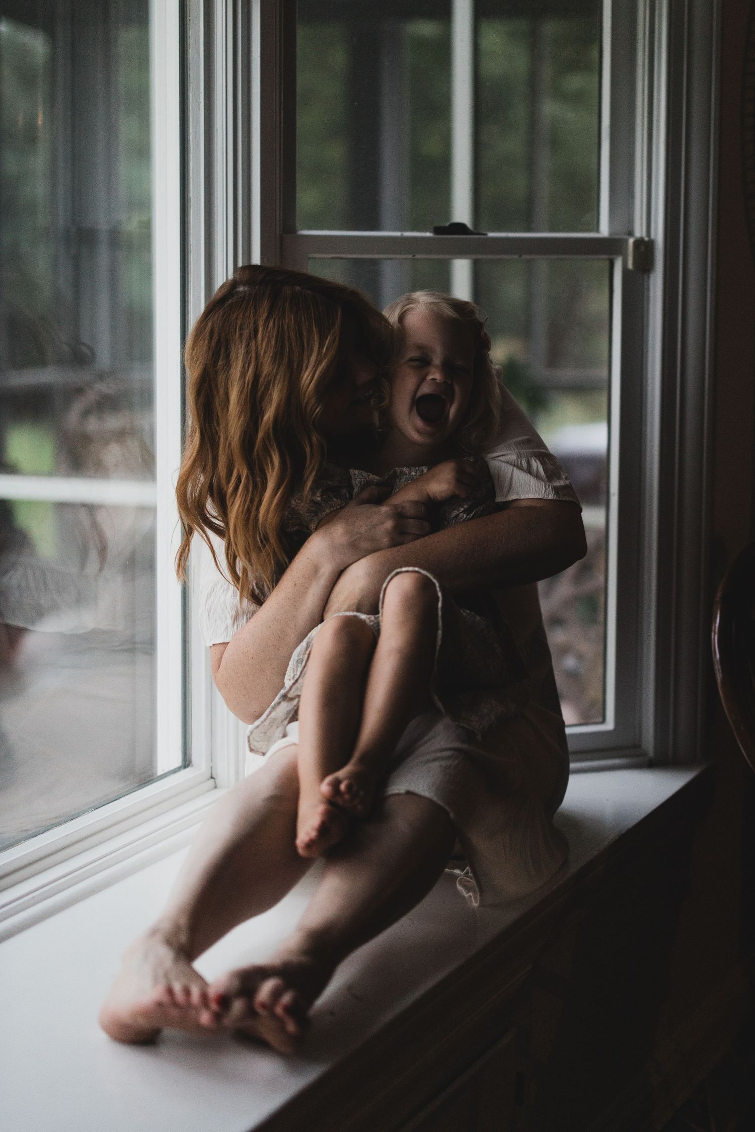 Sun-lit window portrait of parent and child sharing a joyful moment together.