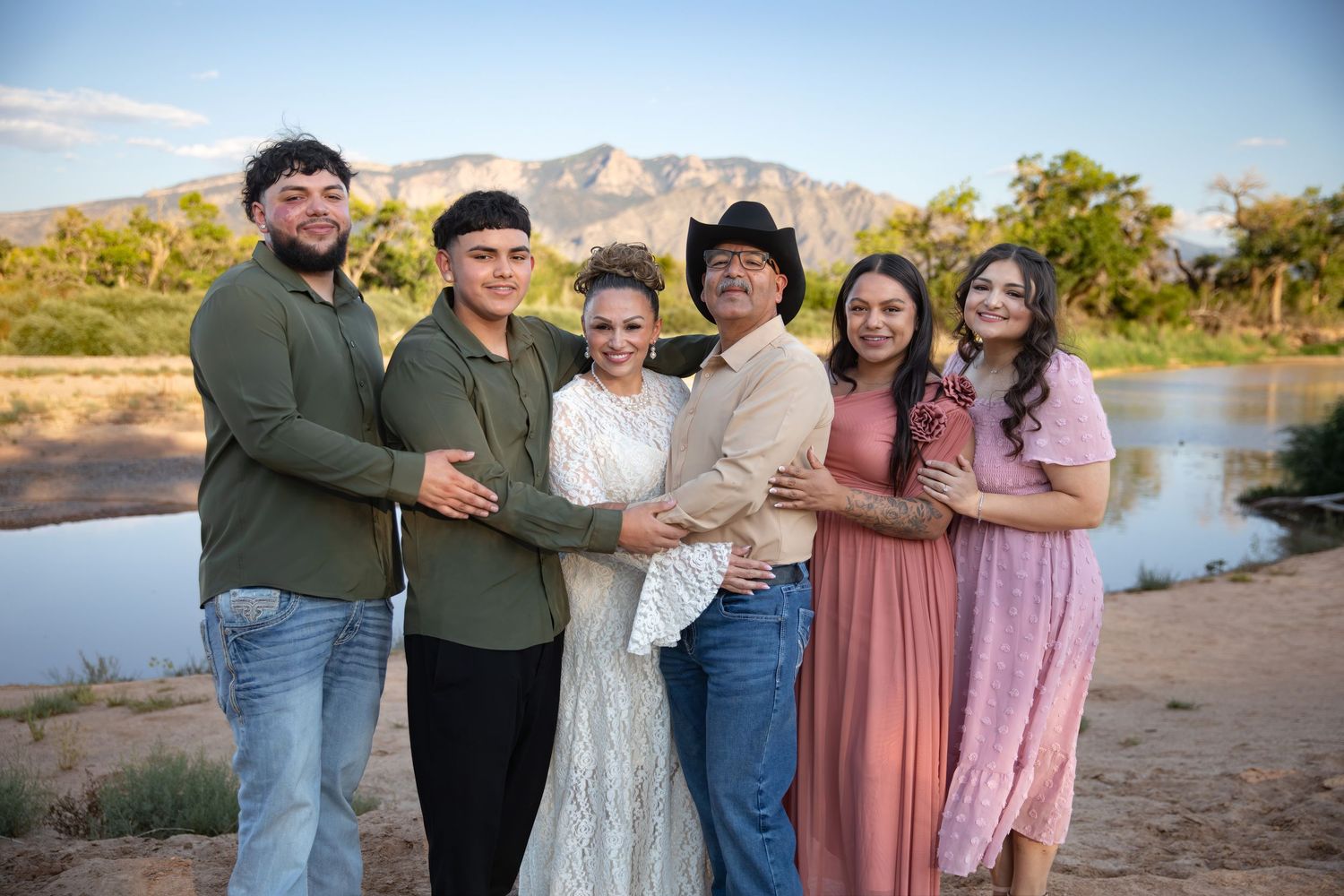 A couple poses together in a desert landscape with mountains and shrubs during golden hour.