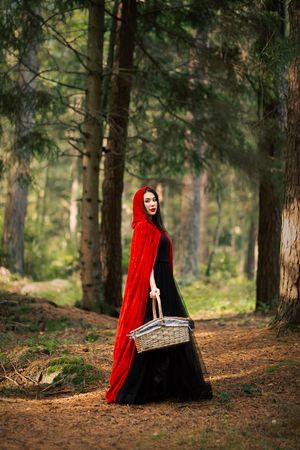 En vacker kvinna som ser ut som Rödluvan går genom skogen och håller i en korg.