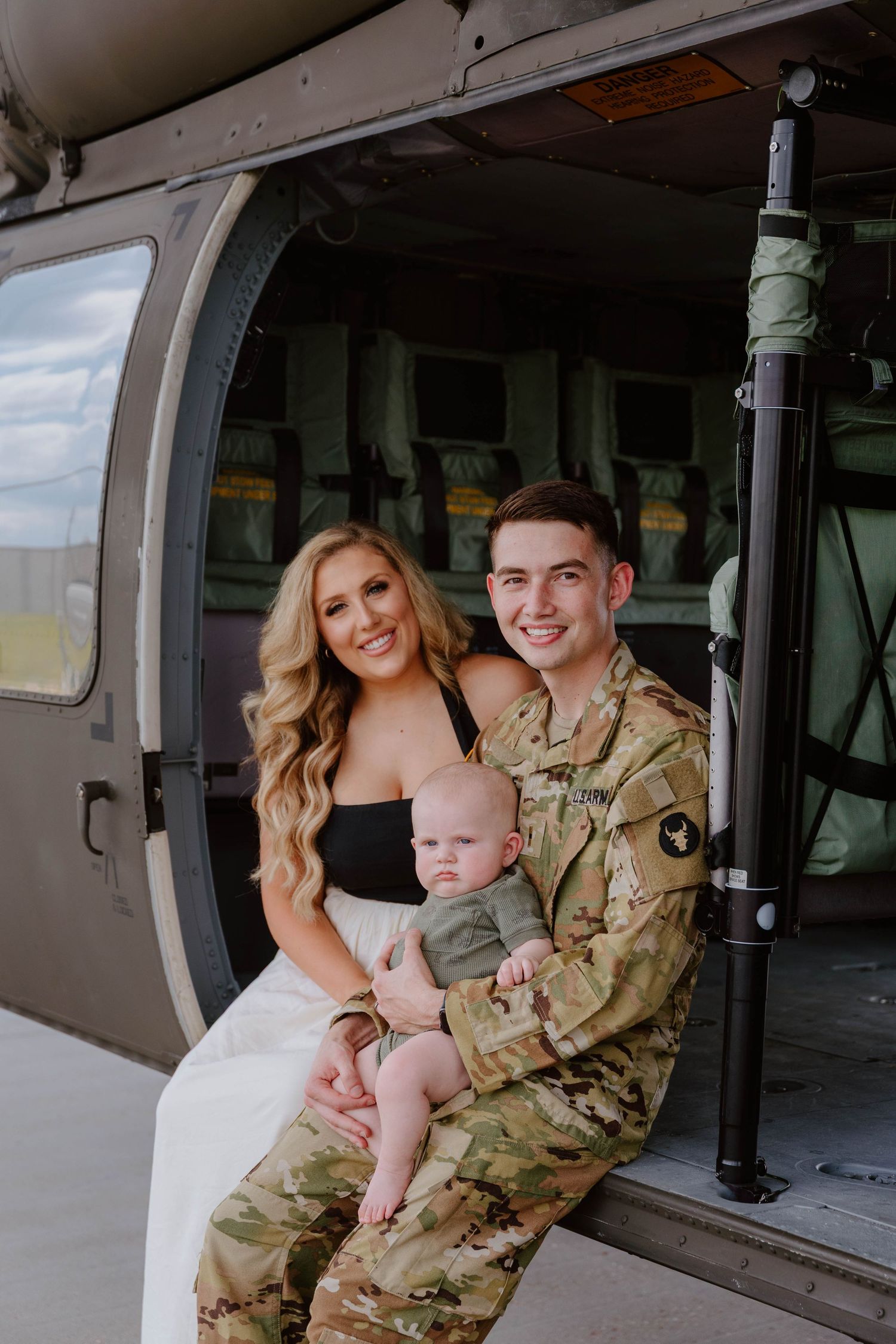 Military family photoshoot inside aircraft hangar with camouflage uniform.