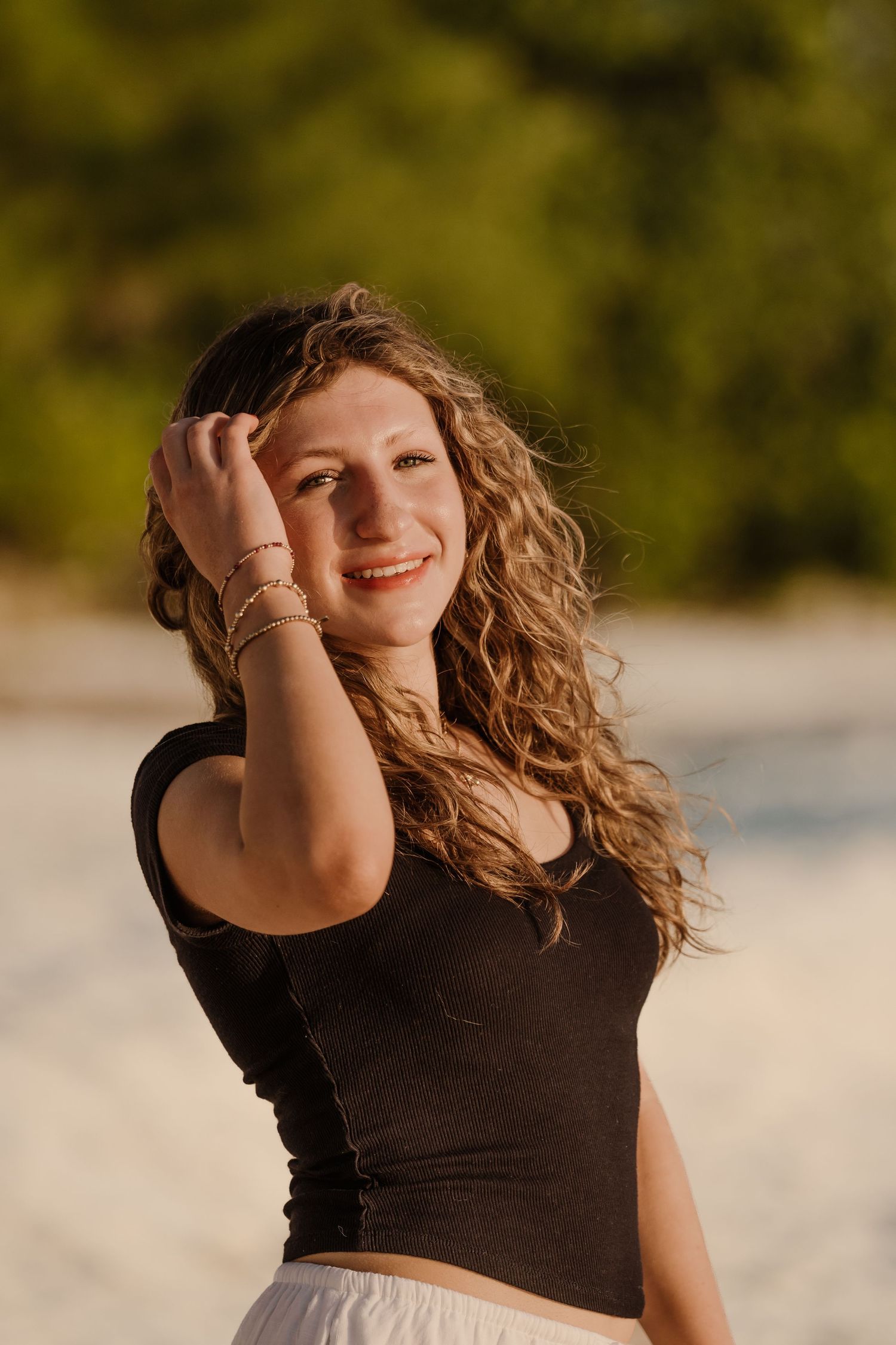 A person with curly hair wearing a black top and white skirt poses outdoors during golden hour at sunset. Senior Photos Grand Cayman