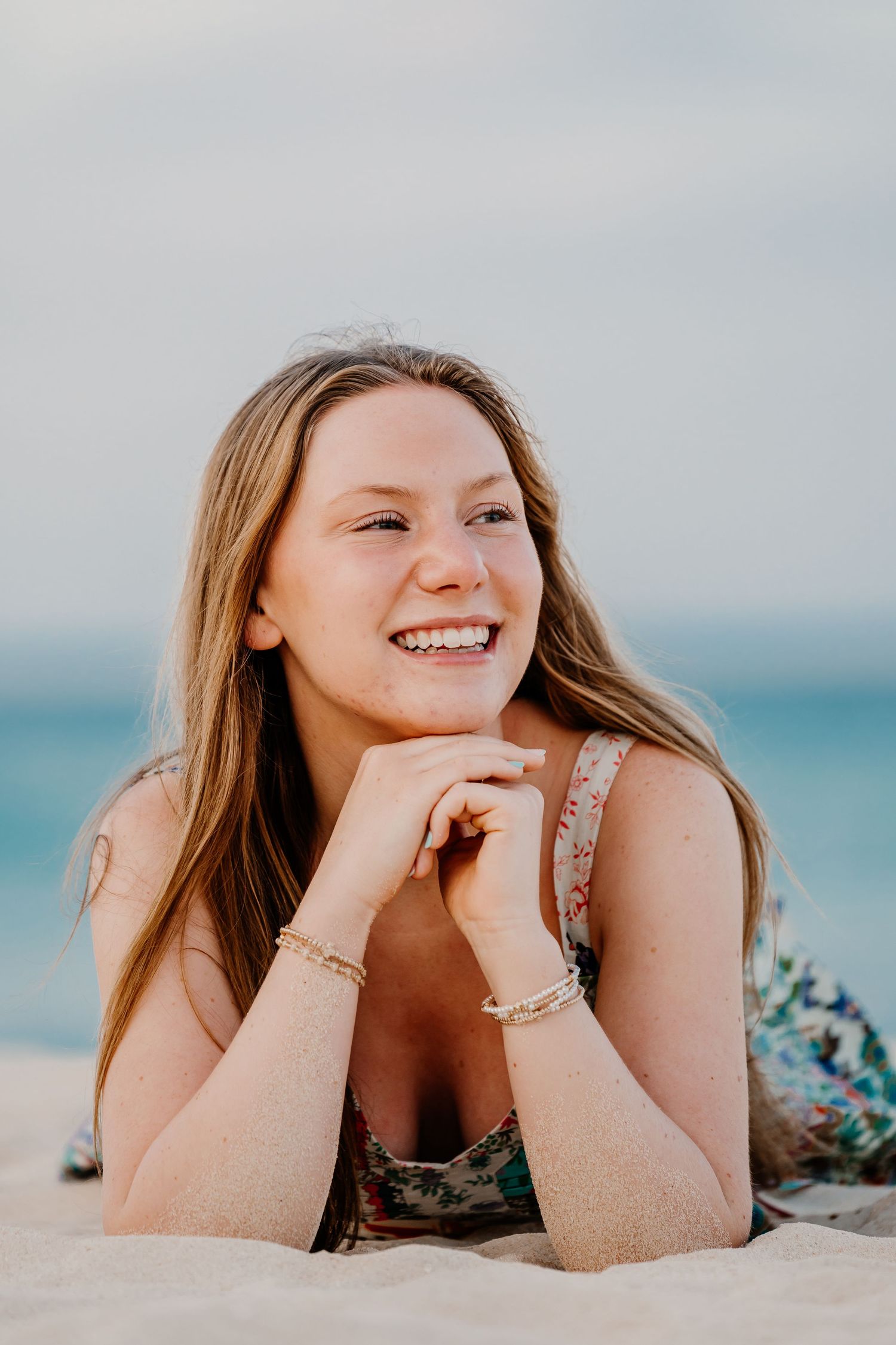 Portrait of someone lying on sandy beach wearing summer outfit with ocean and blue sky in background. Senior Photos