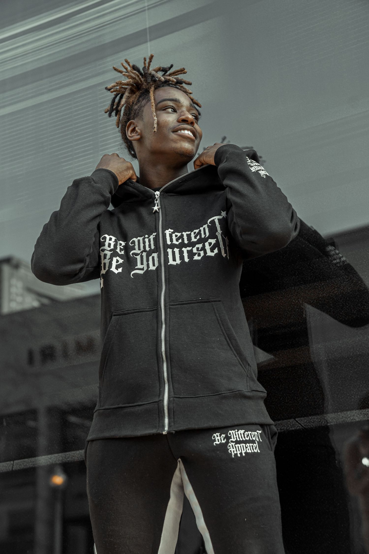 Person wearing black zip-up hoodie with stylish text design poses against grey background.