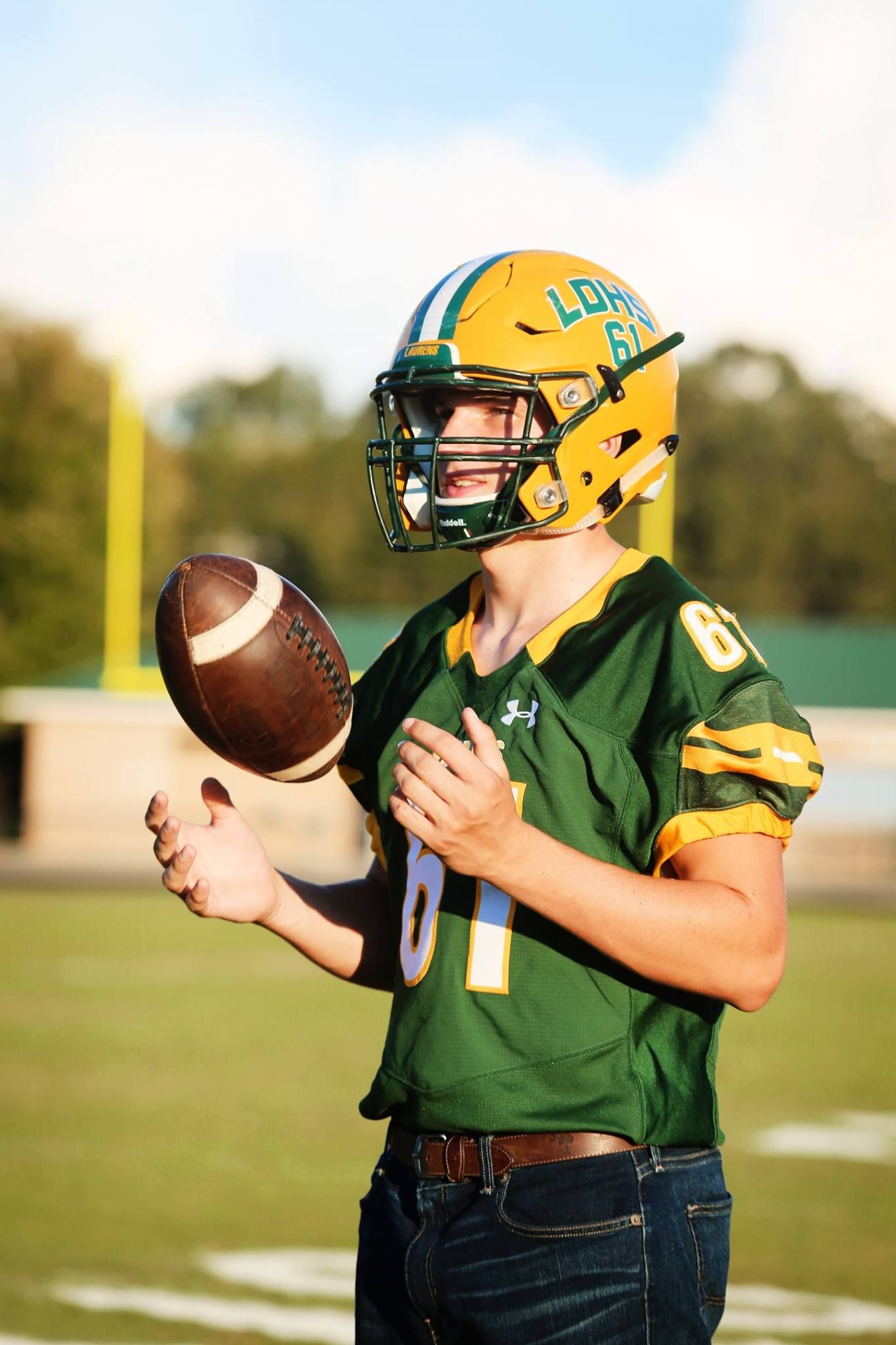 Football player in green and yellow uniform holds ball on field during golden hour.